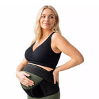 A pregnant woman wearing a black sports bra and a pregnancy belly support band on a white background.