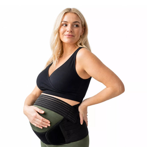 A pregnant woman wearing a black sports bra and a pregnancy belly support band on a white background.